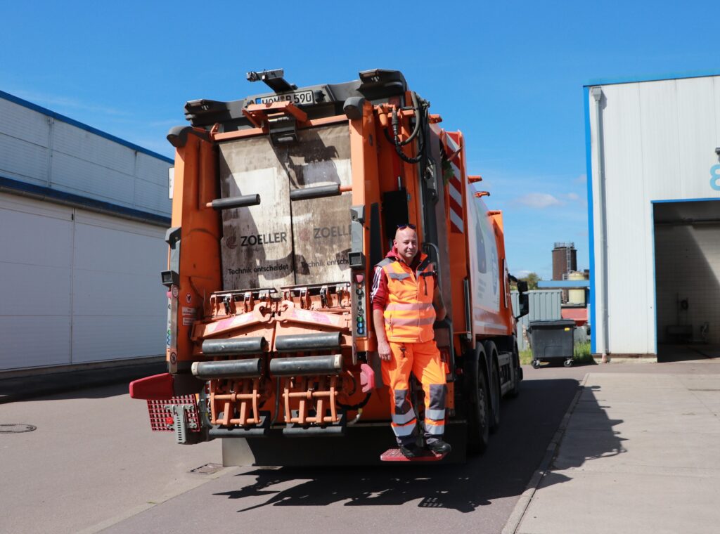 Ein Müllwerker steht auf der Plattform am hinteren Ende des Müllautos